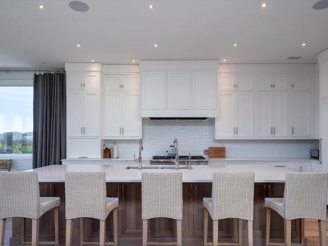kitchen featuring light countertops, decorative backsplash, a center island with sink, and white cabinets