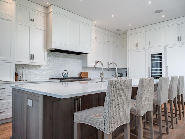 kitchen with tasteful backsplash, an island with sink, and white cabinets