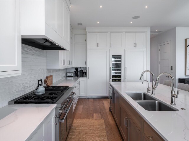 kitchen featuring dark wood-style flooring, high end stainless steel range, premium range hood, white cabinets, and a sink
