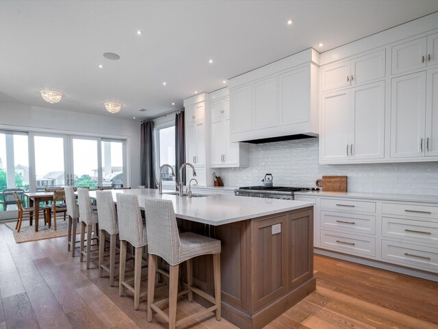 kitchen featuring white cabinets, a breakfast bar, a sink, a kitchen island with sink, and tasteful backsplash