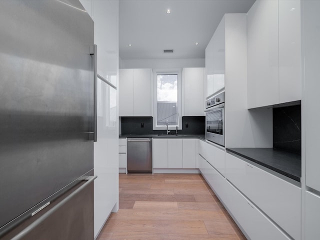 kitchen with dark countertops, modern cabinets, white cabinetry, light wood-style flooring, and appliances with stainless steel finishes