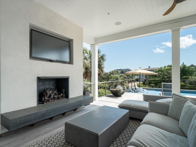 living area featuring floor to ceiling windows, exterior fireplace, a ceiling fan, and wood finished floors