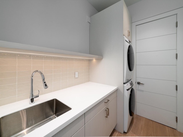laundry room featuring cabinet space, stacked washing maching and dryer, a sink, and light wood finished floors