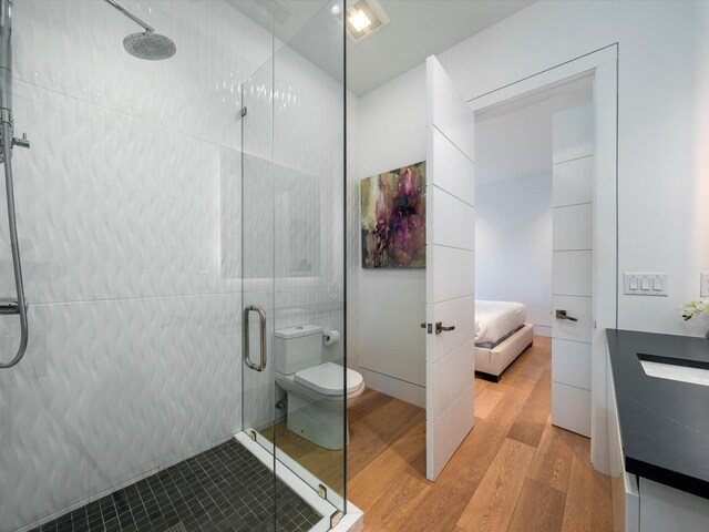 ensuite bathroom with connected bathroom, vanity, toilet, wood finished floors, and a stall shower