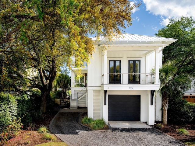 view of front of property featuring a standing seam roof, stairway, a balcony, french doors, and gravel driveway