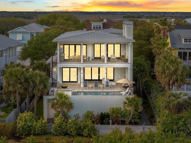 back of house featuring a chimney, a fenced in pool, fence, a balcony, and stairs