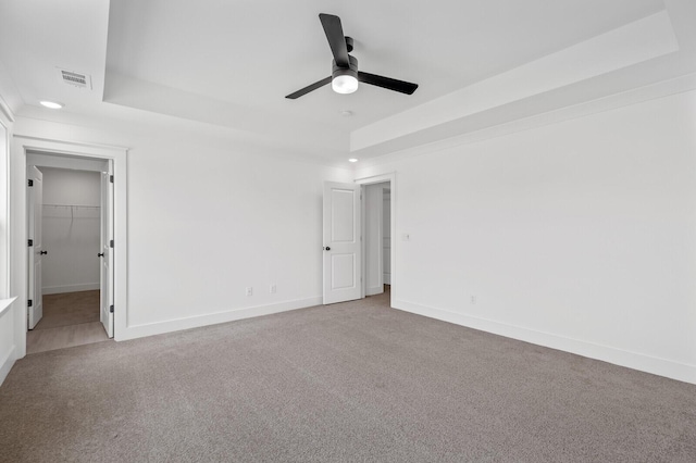 unfurnished bedroom featuring a walk in closet, ceiling fan, a tray ceiling, carpet floors, and a closet