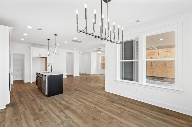 kitchen with ceiling fan, sink, hanging light fixtures, dark wood-type flooring, and a kitchen island with sink