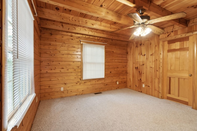 carpeted spare room featuring beamed ceiling, ceiling fan, wooden ceiling, and wooden walls