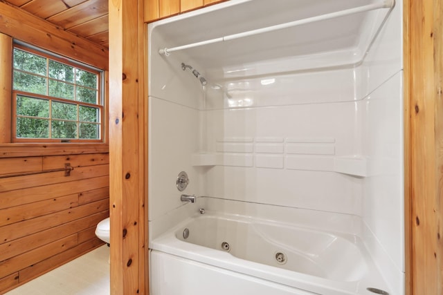 bathroom with bathing tub / shower combination, wooden walls, and toilet