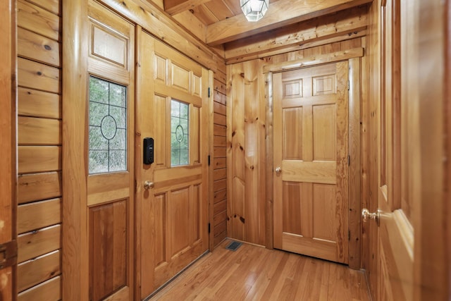 entryway featuring beam ceiling, light wood-type flooring, and wood walls