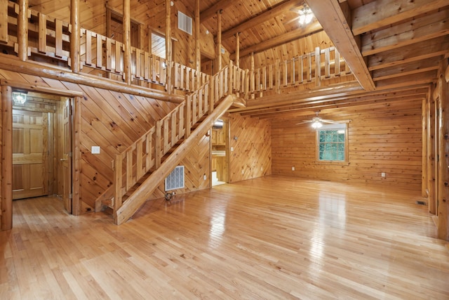 unfurnished living room featuring beam ceiling, wooden walls, wood-type flooring, and a towering ceiling