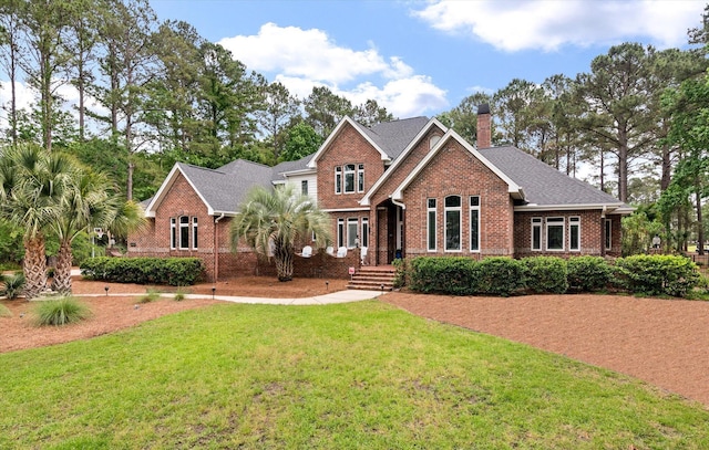 view of front facade featuring brick siding, a front yard, a chimney, and a shingled roof