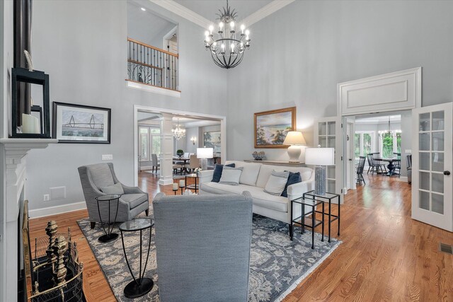 living area with a chandelier, a towering ceiling, baseboards, wood finished floors, and french doors