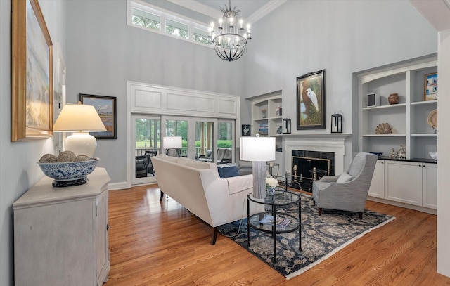 living room featuring a chandelier, a high ceiling, a fireplace, light wood-type flooring, and crown molding