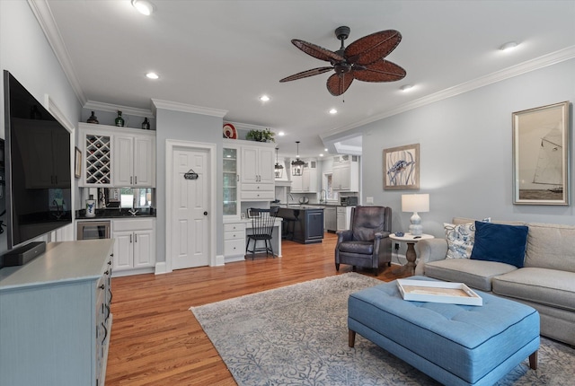 living room featuring a ceiling fan, light wood-style floors, crown molding, wine cooler, and recessed lighting