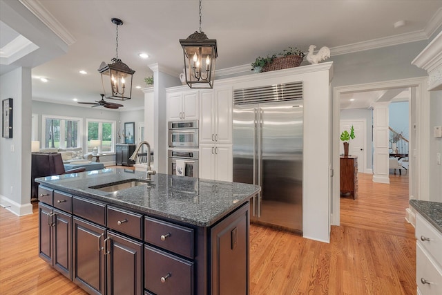 kitchen featuring stainless steel appliances, a sink, white cabinets, decorative columns, and a chandelier