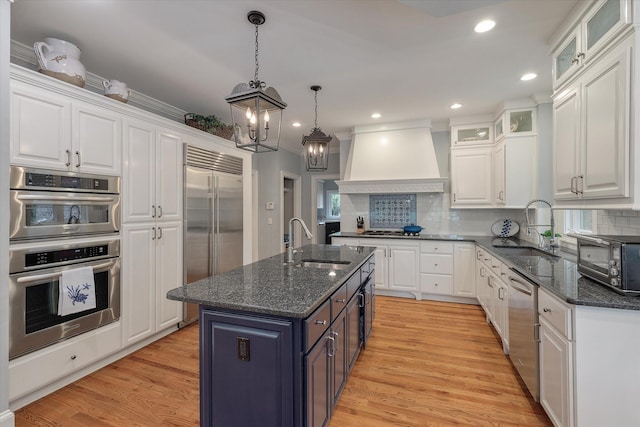 kitchen with stainless steel appliances, custom range hood, a sink, white cabinetry, and recessed lighting