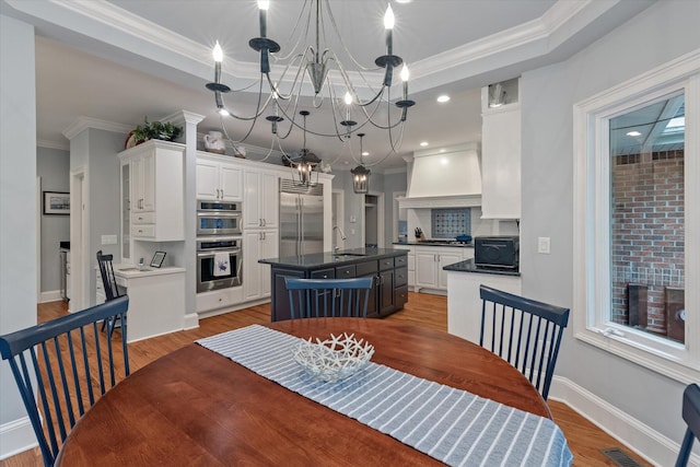 dining space featuring a chandelier, crown molding, wood finished floors, a tray ceiling, and baseboards