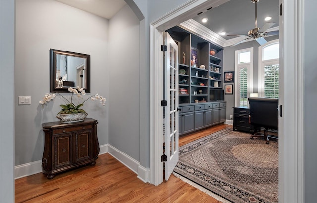 office area featuring light wood finished floors, a ceiling fan, arched walkways, baseboards, and ornamental molding