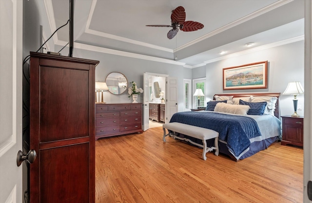 bedroom featuring a tray ceiling, light wood-style floors, ensuite bath, ornamental molding, and ceiling fan