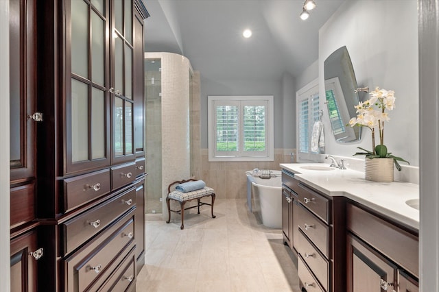 bathroom with tile walls, a freestanding tub, vaulted ceiling, double vanity, and a wainscoted wall