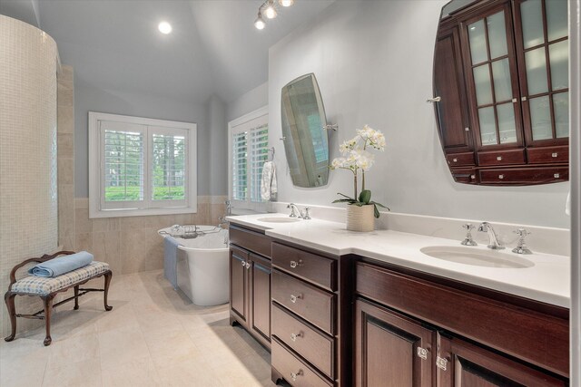 full bathroom with tile walls, vaulted ceiling, a freestanding bath, double vanity, and tile patterned floors