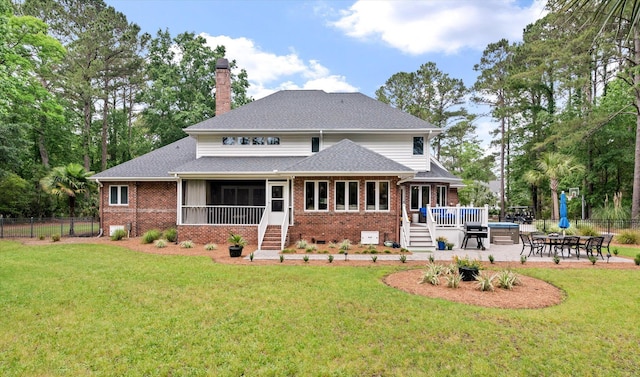 rear view of house with brick siding, a wooden deck, a chimney, a patio area, and a shingled roof