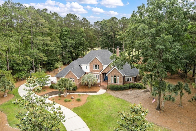 traditional home with brick siding, a chimney, a front yard, curved driveway, and a shingled roof