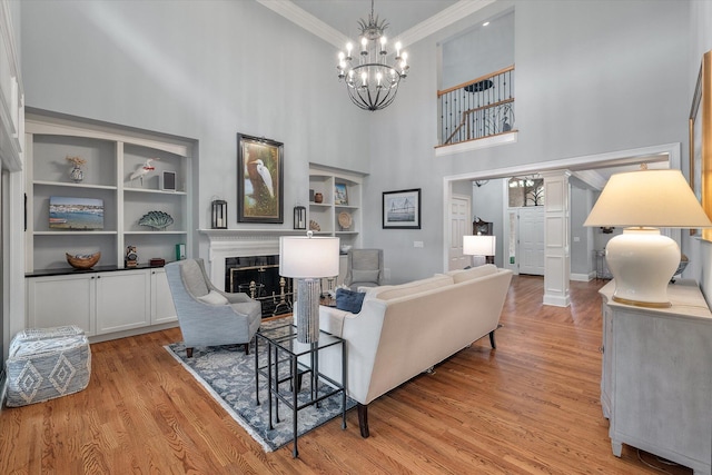 living room featuring a chandelier, a towering ceiling, light wood-style flooring, crown molding, and a fireplace