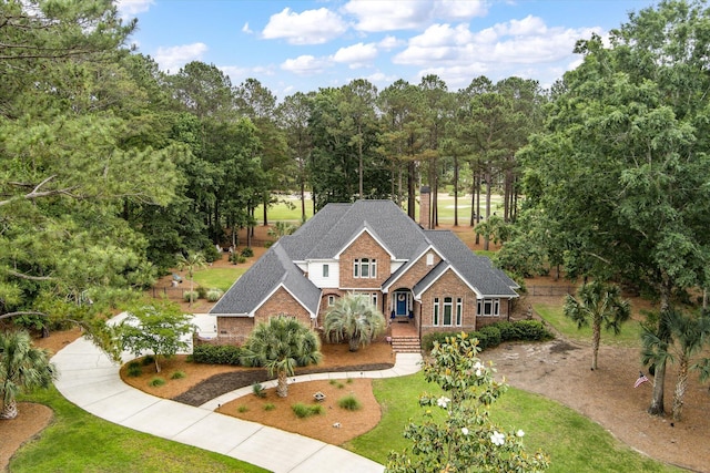 view of front of property with brick siding, roof with shingles, a front yard, and view of scattered trees