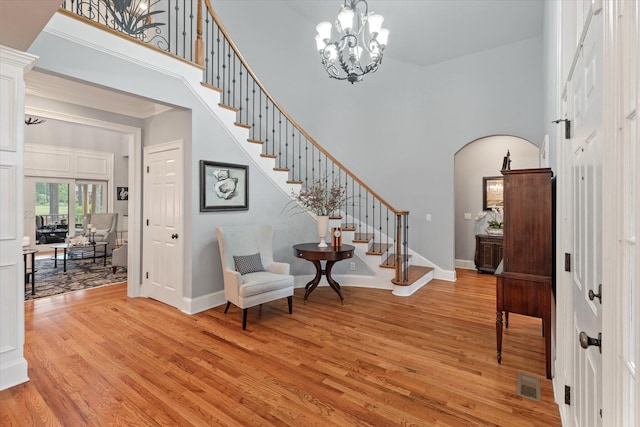 entryway with stairs, a towering ceiling, light wood finished floors, arched walkways, and baseboards