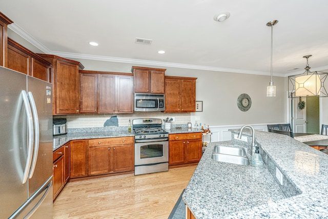 kitchen with appliances with stainless steel finishes, pendant lighting, sink, crown molding, and light stone countertops