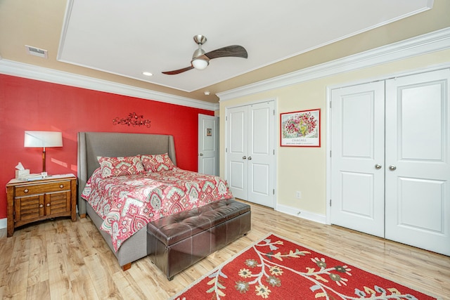 bedroom with hardwood / wood-style flooring, ceiling fan, ornamental molding, and two closets