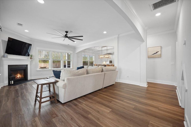 living area featuring arched walkways, dark wood-style floors, ceiling fan with notable chandelier, and a fireplace with flush hearth