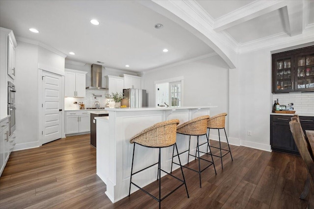 kitchen with dark wood-type flooring, a kitchen bar, light countertops, stainless steel appliances, and wall chimney exhaust hood