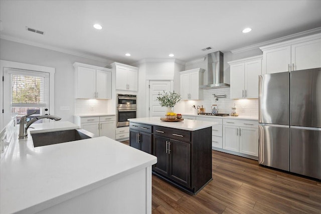 kitchen with visible vents, appliances with stainless steel finishes, white cabinetry, wall chimney exhaust hood, and a sink