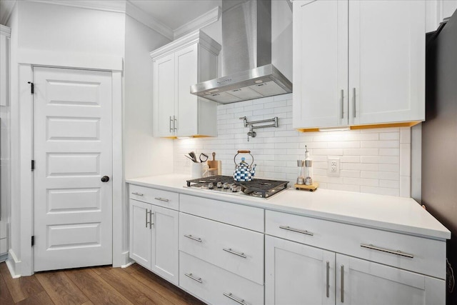 kitchen featuring dark wood-type flooring, stainless steel gas cooktop, ornamental molding, white cabinets, and wall chimney exhaust hood