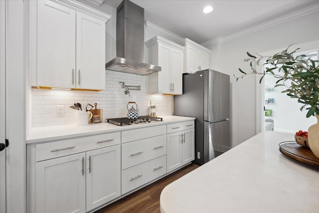 kitchen featuring crown molding, wall chimney range hood, light countertops, white cabinets, and stainless steel appliances