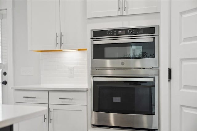 kitchen featuring tasteful backsplash, double oven, light countertops, and white cabinetry