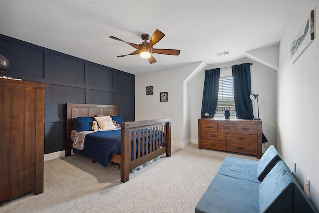 bedroom featuring baseboards, visible vents, ceiling fan, light carpet, and a decorative wall