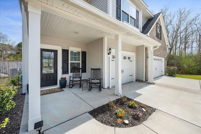 property entrance with central air condition unit, an attached garage, covered porch, and driveway