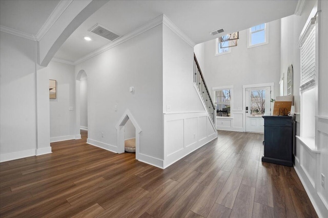 unfurnished living room with crown molding, dark wood-style floors, arched walkways, and visible vents