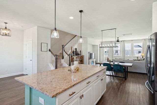 kitchen featuring stainless steel fridge, white cabinets, a chandelier, hanging light fixtures, and a center island