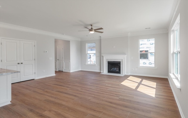 unfurnished living room featuring ornamental molding, wood finished floors, a fireplace with flush hearth, and a wealth of natural light