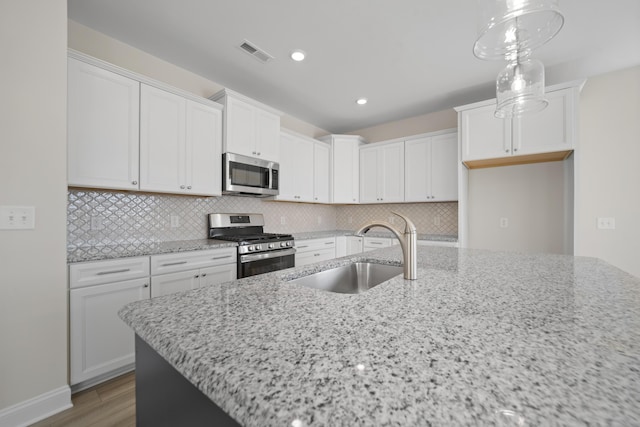 kitchen featuring visible vents, decorative backsplash, light stone countertops, stainless steel appliances, and a sink