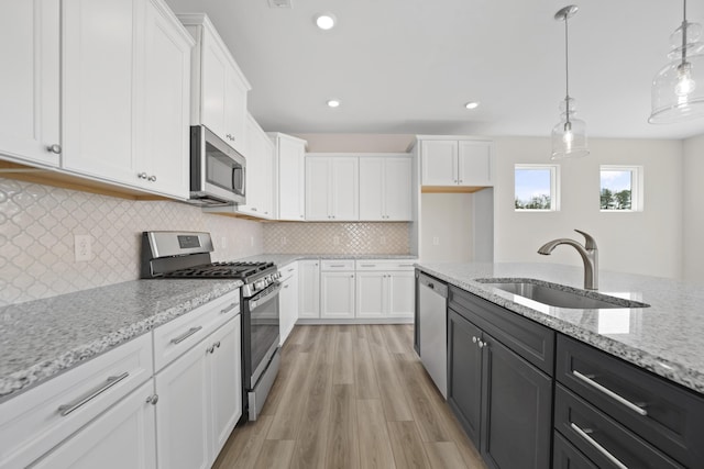 kitchen with pendant lighting, stainless steel appliances, white cabinets, a sink, and light wood-type flooring