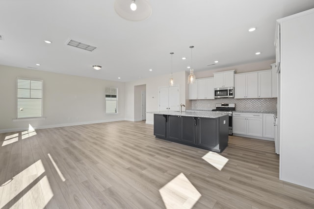 kitchen featuring stainless steel appliances, tasteful backsplash, visible vents, open floor plan, and white cabinets