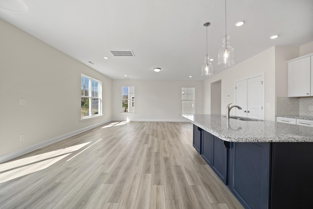 kitchen featuring tasteful backsplash, visible vents, light wood-style floors, a sink, and baseboards