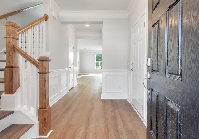 foyer featuring a wainscoted wall, ornamental molding, wood finished floors, and stairs